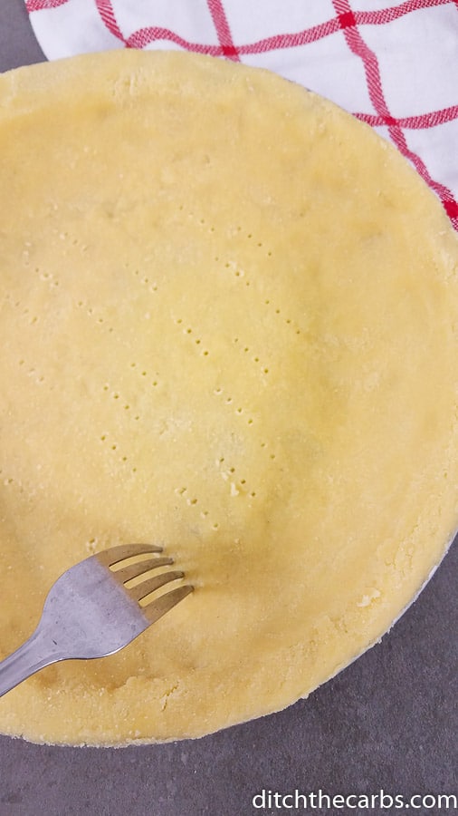 Coconut flour pie crust being poked with a fork