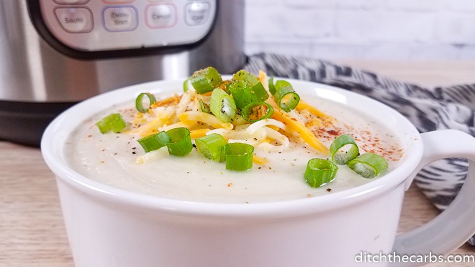 Creamy cauliflower soup garnished with shredded cheese and sliced spring onions