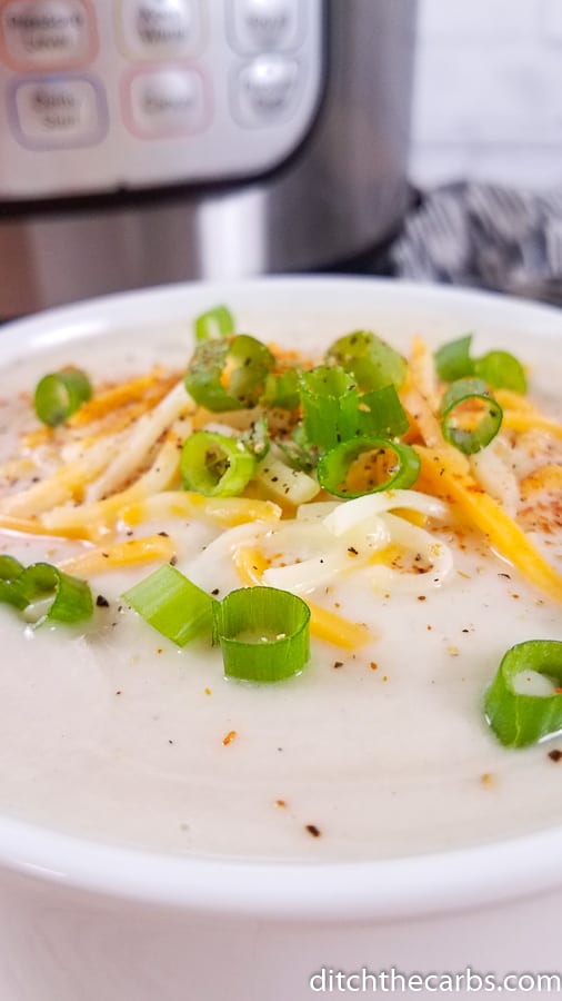 Creamy cauliflower soup garnished with shredded cheese and sliced spring onions