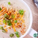 Creamy cauliflower soup served in a white mug garnish with spring onions and cheese
