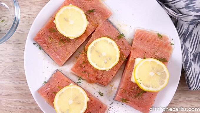 salmon sitting on a white plate with slices of lemon
