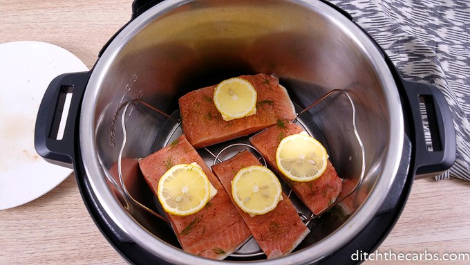 Raw salmon with dill and a lemon slice sitting on a trivet inside and instant pot
