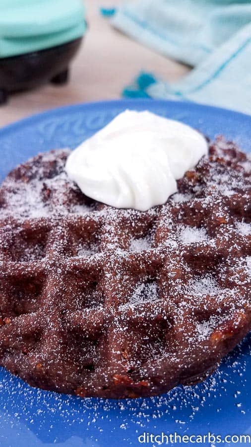 chocolate chaffle sitting on a blue plate with whipped cream and sweetener sprinkled