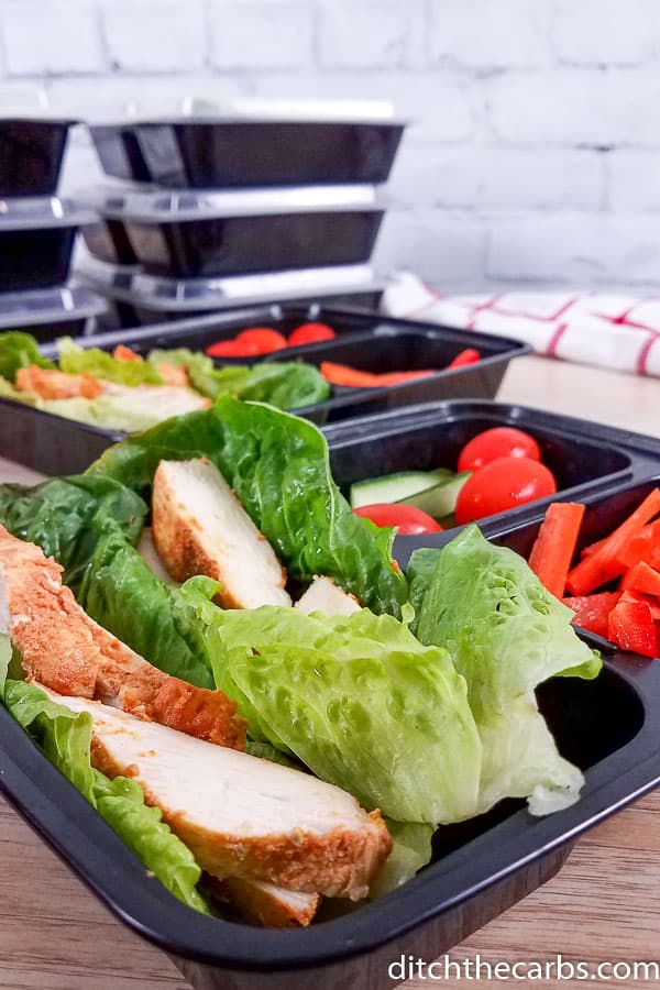 Meal prep containers with lettuce and cook chicken plus tomatoes and peppers