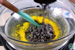 A bowl of cake batter with sugar free chocolate chips being poured inside