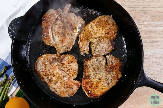 Cast iron skillet with pork chops being fried