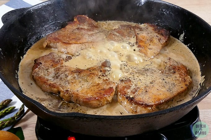 Cast iron skillet with pork chops and a creamy sauce