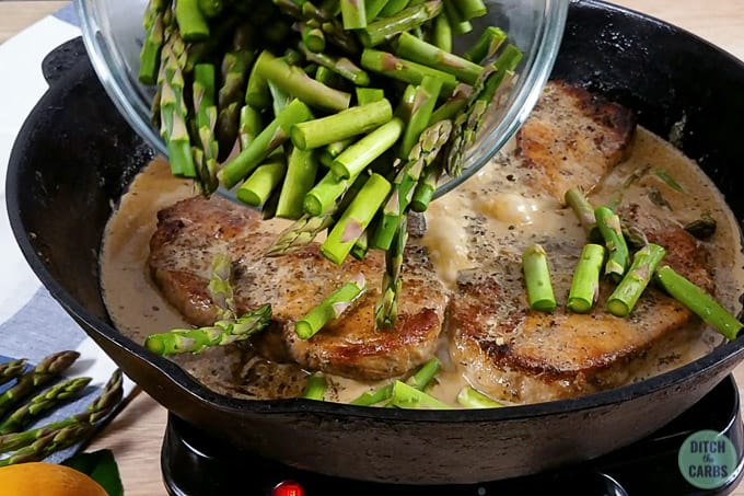 Cast iron skillet with pork chops and pieces of chopped asparagus