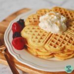 waffles stacked on a plate with whipped cream and berries