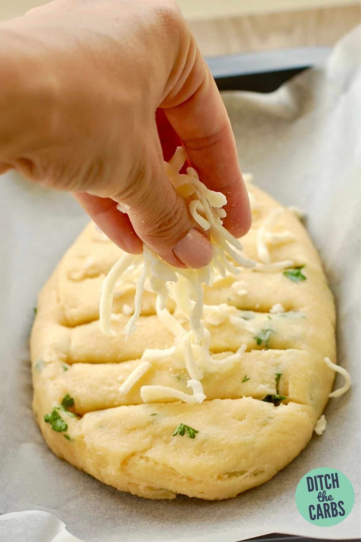 hands sprinkling shredded cheese onto garlic bread