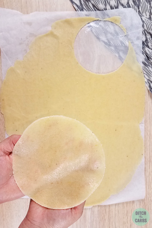 One keto tortilla being cut from rolled out mozzarella dough.