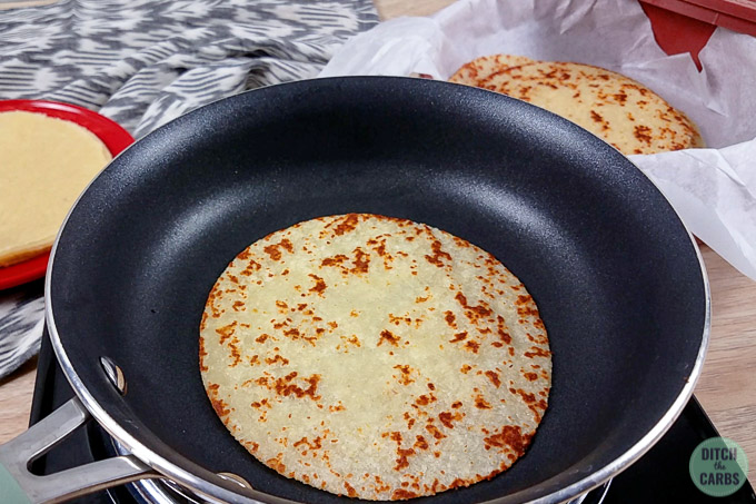 One keto tortilla cooking in a pan.