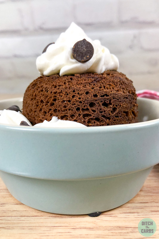 Chocolate keto mug cake in a light blue dish with whipped cream and chocolate chips on top.