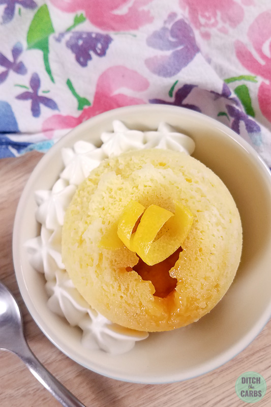 Above view of a lemon curd low-carb mug cake in a dish with whipped cream on the side.
