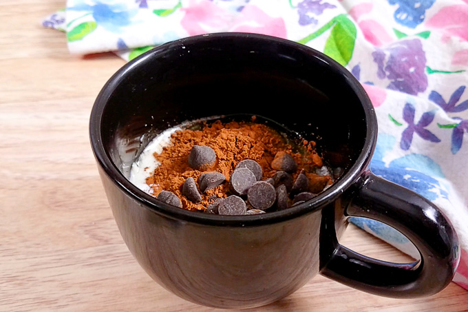 All the ingredients for a double chocolate low-carb mug cake in a black mug. Ingredients are not mix.