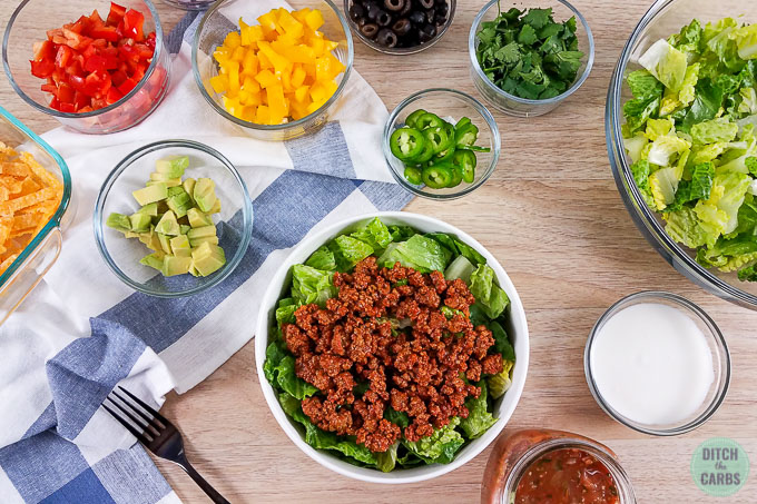 Low-Carb Taco Salad and toppings in glass bowls on top of blue and white towel on wooden table