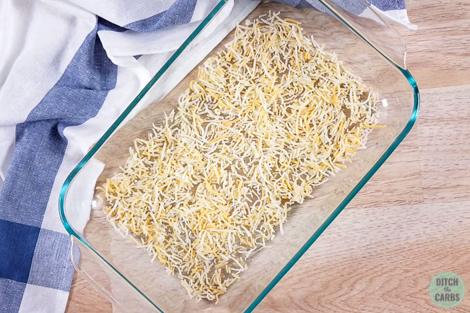 Shredded cheese spread out in a glass baking pan getting ready to bake for low-carb taco salad.