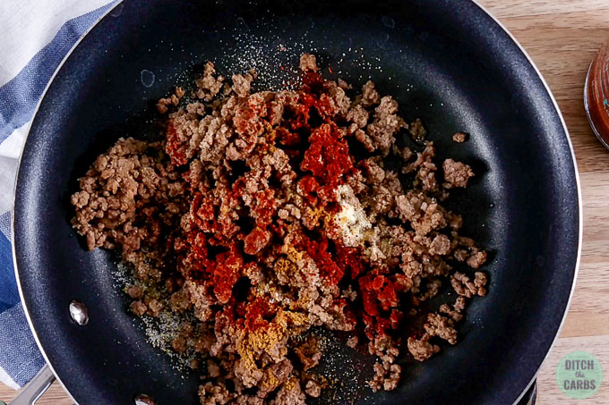 Adding seasoning to cooked ground beef in a skillet.