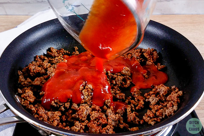 Pour tomato sauce over cooked and seasoned ground beef in a skillet.