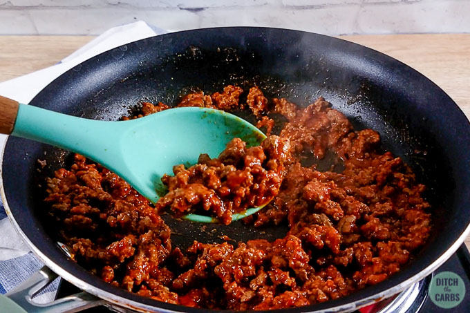 Taco meat for low-carb taco salad being cooked in a skillet. A spoon is scooping some of the cooked taco meat.