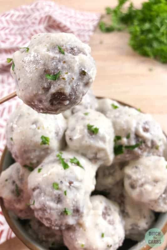 Creamy goat cheese keto meatballs in a bowl. One meatball is being lifted by a toothpick.