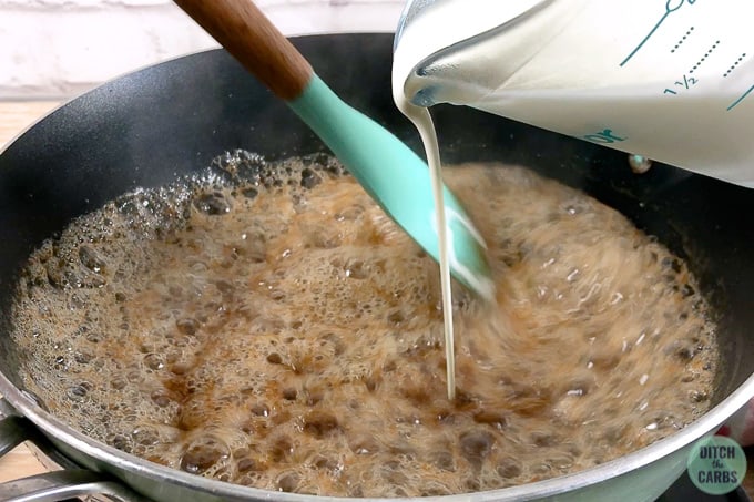Pour heavy cream into the melted brown sweetener and butter to make caramel. The contents are in a skillet on the stove.