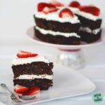 Low carb chocolate zucchini cake with whipped cream and berries on a white plate with strawberries