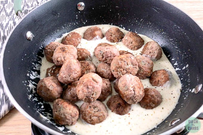 Creamy goat cheese sauce in the pan with cooked keto meatballs added to the pan.