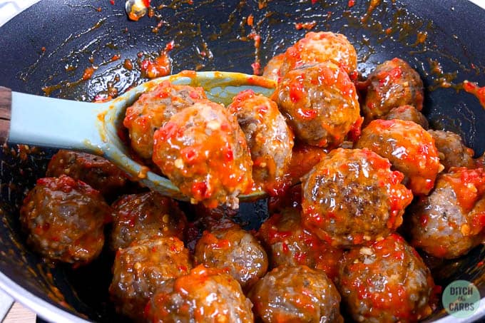 Keto meatballs tossed in a spicy garlic sauce. The meatballs are in a black skillet and are being lifted with a light green spoon.