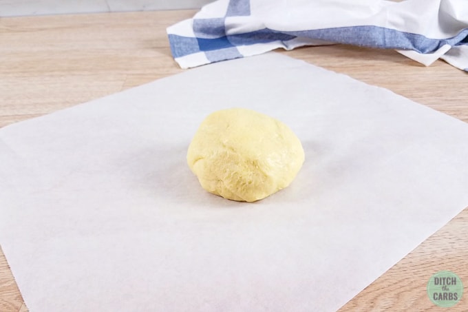 Fat Head dough in a ball in the middle of a piece of parchment paper ready to be rolled out.