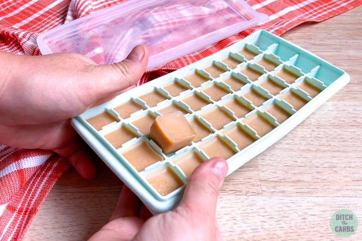 Two hands pushing one fudge square up in the light green silicone ice cube tray to remove the hardened fudge from the tray.