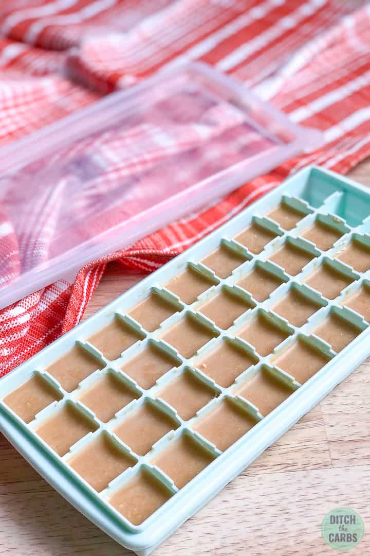 Hardened keto peanut butter fudge in a light green silicone ice cube tray with a clean lid next to it and an orange towel off to the side.