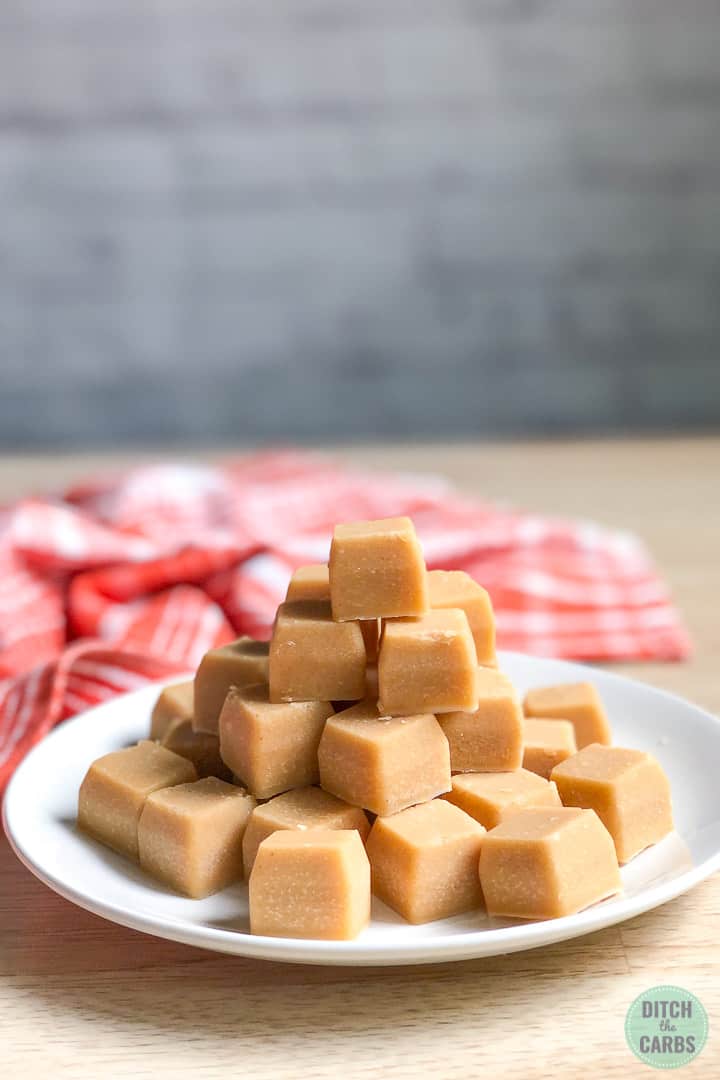 Keto peanut butter fudge stacked in a pyramid on a white plate. An orange dish towel is in the background.