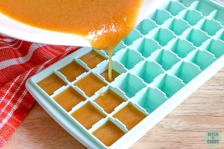 Keto peanut butter fudge mixture is poured from the white bowl into a light green silicone ice cube tray.