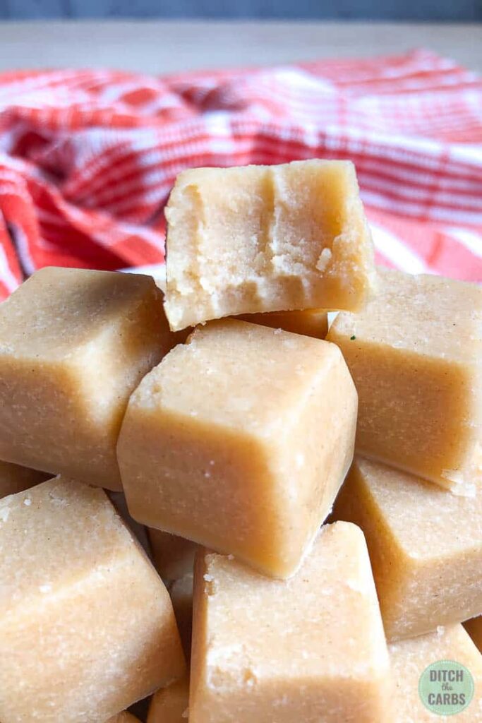 Close up picture of finished keto peanut butter fudged removed from the ice cube tray and stacked on a plate. The top fudge square has a bite taken out of it.
