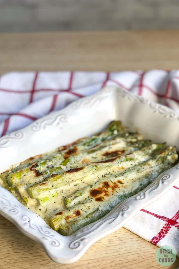 Keto cheesy baked asparagus in a white dish resting on a red and white checkered napkin.