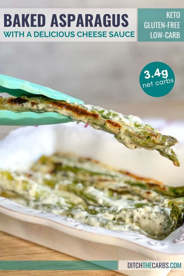 Keto cheesy baked asparagus being lifted from a white baking pan by light green tongs.