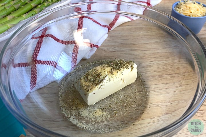 A piece of cheese and herbs in a glass mixing bowl