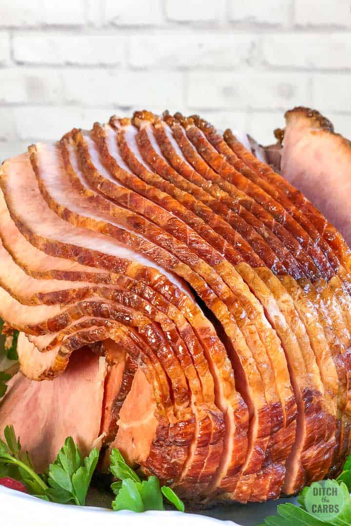 A close-up image of hams cooked in a white baking pan.  There is green parsley underneath the ham as an ornament.