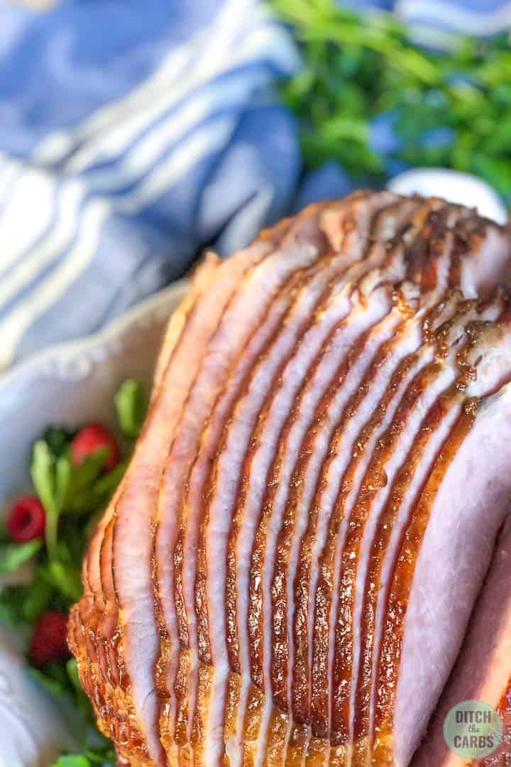 Close up image of the ham slices and cooked in a white baking pan with a blue napkin in the background. The glaze on the ham is glossy.