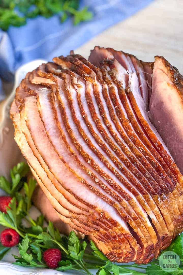 Close up overhead image of the ham slices and cooked in a white baking pan with a blue napkin in the background.