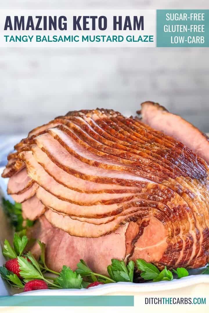 Keto ham cooked, sliced, and ready to serve in a white serving dish. Green parsley and red raspberries garnish the baking dish.