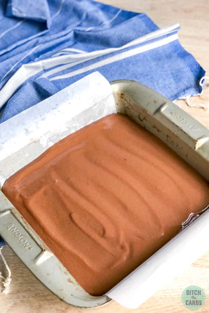 Dairy-free brownie batter spread out in a square metal baking pan lined with white parchment paper.