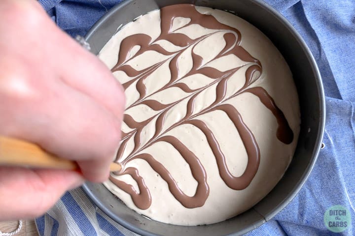 Making a chocolate swirl on top of the cheesecake with a chopstick.