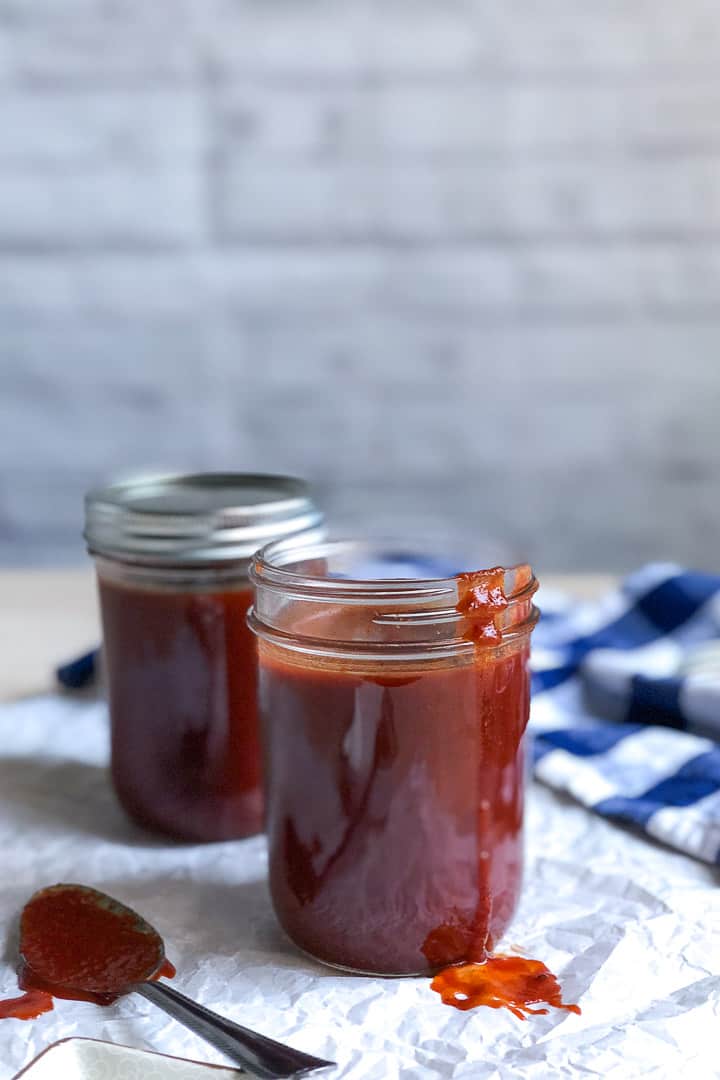 Two jars of keto BBQ sauce. One jar is opened with a drip of BBQ sauce sliding down the jar.