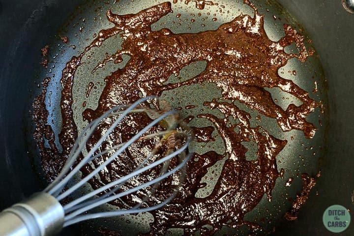 Olive oil, spices, and sweetener melted together in a sauce pan being stirred by a whisk.