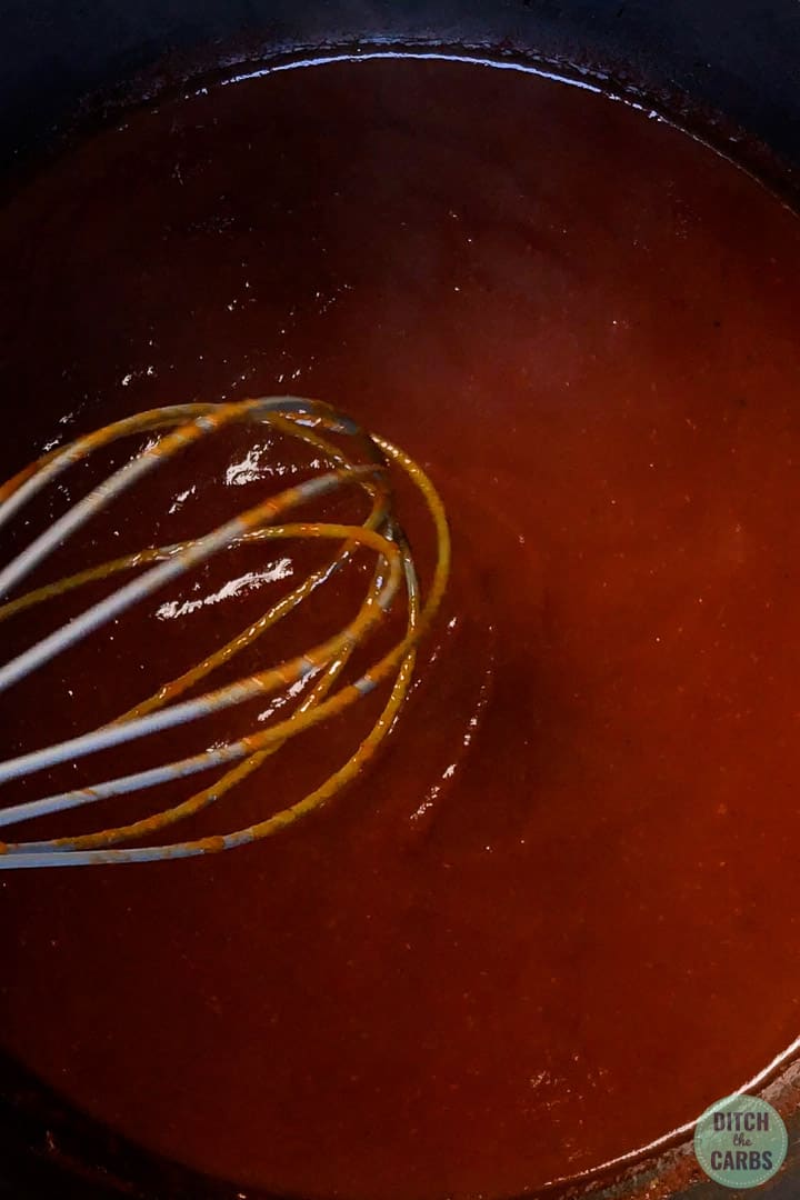 Close up image of keto BBQ sauce being stirred in a saucepan with a whisk.