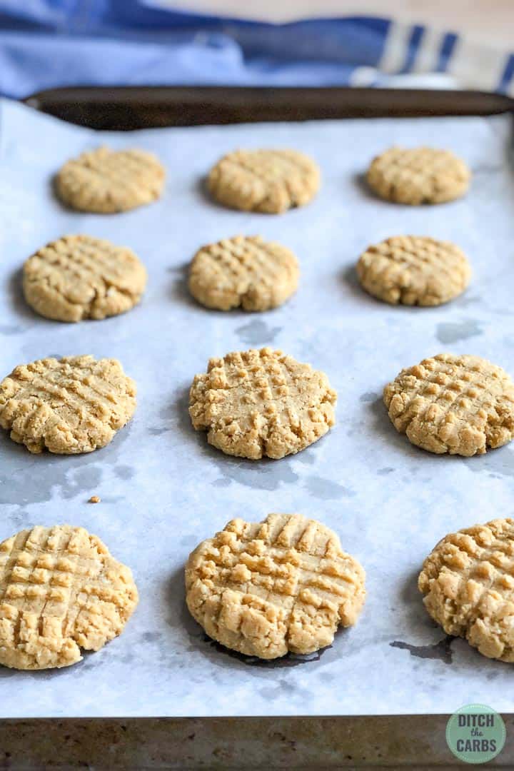 Cooked keto peanut butter cookies cooling on a baking sheet lined with white parchment paper.