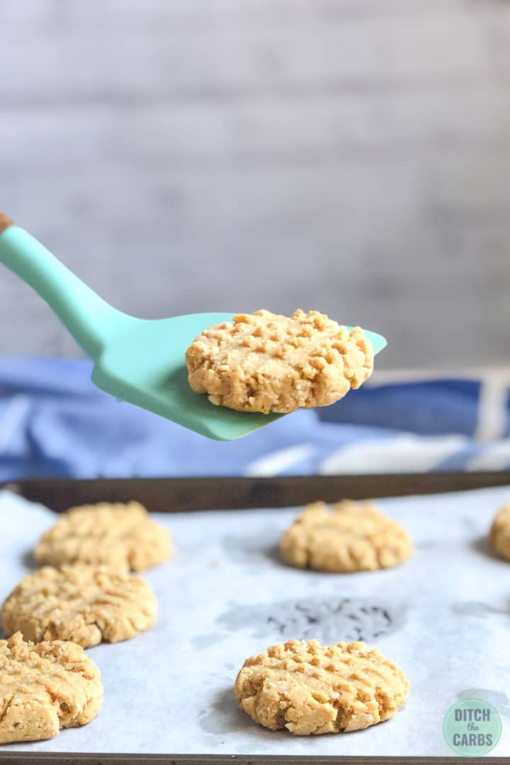 A cookie is being lifted on a light green spoon from the baking sheet.