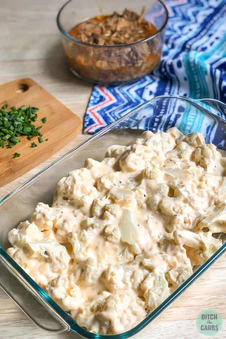 The cauliflower has been tossed in the cheese sauce and then transferred to a clear glass casserole dish.